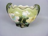 a green vase with flowers on it on a white surface