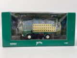 un petit camion jouet vert et jaune dans une boîte verte posée sur une surface blanche