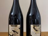 two bottles of red wine sitting on top of a wooden table