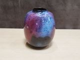 purple and blue vase sitting on top of a wooden table next to a wall