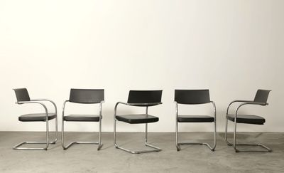 quatre chaises noires sont alignées contre un mur blanc
