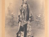 an old photo of a woman in a kimono standing in front of a bush