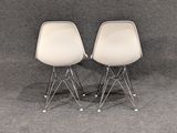 pair of white eames chairs with chrome legs on a grey background