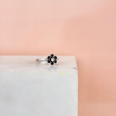 a close up of a black diamond flower ring on a white marble block