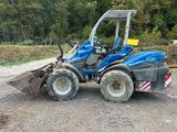 a blue tractor is parked on a gravel road near a forest