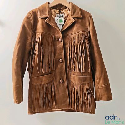 une veste en daim marron avec des franges, suspendue à un cintre