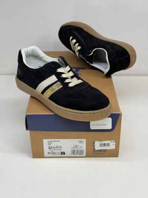des baskets noires et dorées avec des lacets blancs, posées sur une boîte en carton