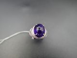 une image représentant une bague ornée d'une pierre violette sur un fond noir