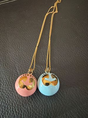 deux colliers posés sur un fond noir, composés d'une chaîne dorée et d'une boule rose et bleue