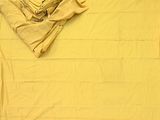 a bed with a yellow comforter and a stack of folded sheets