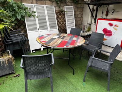 a table and chairs in the yard with a painting on the wall