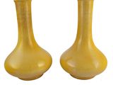 une paire de vases jaunes posés sur une surface blanche, sur fond blanc