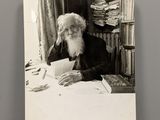photographie en noir et blanc d'un vieil homme assis à une table avec un livre