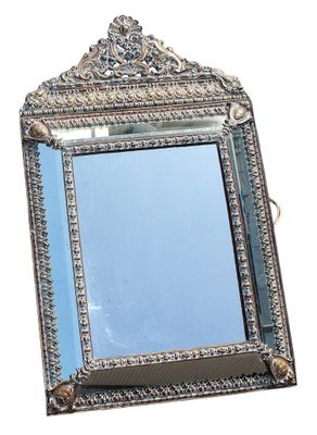 miroir argenté orné d'un motif décoratif sur le dessus, posé sur une surface blanche
