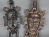 Voici deux masques africains exposés sur une surface grise