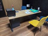 Des chaises aux couleurs vives sont disposées devant un bureau en bois sur lequel se trouve une imprimante