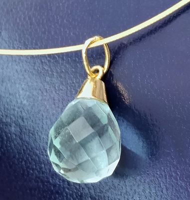 a close up of a necklace with a blue stone on a blue surface