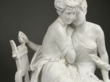 statue of two women sitting on a bench with a bird in their hand