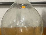 un grand vase en verre posé sur une table, à côté d'une bouteille contenant un liquide