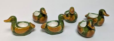 six ceramic ducks are lined up in a row on a white surface