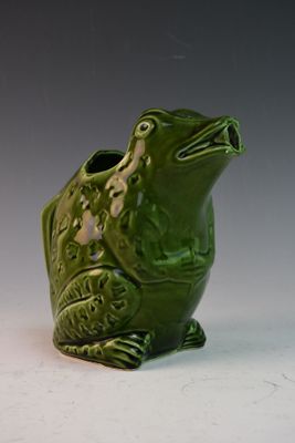 un vase en forme de grenouille verte posé sur une surface blanche