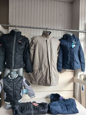 many coats and jackets hanging on a rack in a room