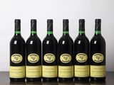 six bouteilles de vin sont posées sur une table devant un mur blanc