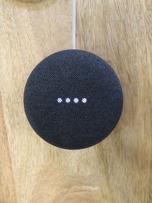 une photo d'une enceinte Google Home noire posée sur une surface en bois