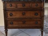 a wooden chest of drawers with marble top on a tile floor