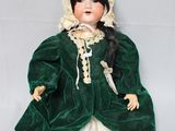 Une vieille poupée vêtue d'une robe verte et d'un bonnet est allongée sur une surface blanche.