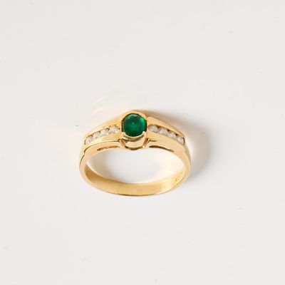 gros plan d'une bague en or avec une pierre verte et des diamants