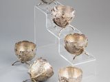 four silver bowls are stacked on a clear stand on a gray background