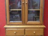 a wooden china cabinet with glass doors and a red wall
