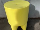 a yellow stool sitting on the sidewalk next to a white wall