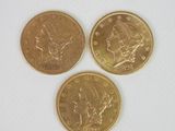 trois pièces d'or posées l'une à côté de l'autre sur une surface blanche