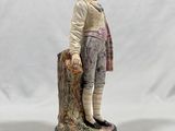 figurine of a boy standing on a stump with a hat on