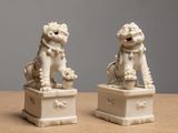 pair of white foo foo statues on a table against a gray background