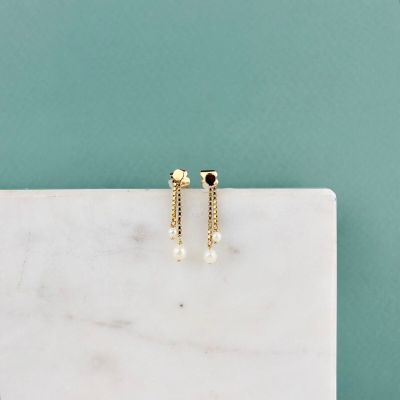 une paire de boucles d'oreilles en or ornées de perles, posées sur une surface en marbre