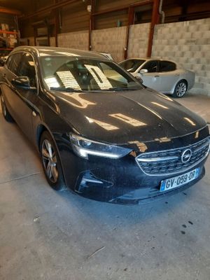 Une voiture noire est garée dans un garage, avec d'autres voitures en arrière-plan.