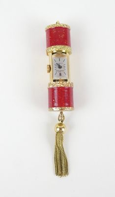 une image représentant une montre rouge et dorée à laquelle est suspendu un pompon sur le côté