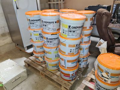 Plusieurs seaux de peinture sont empilés sur une palette dans un entrepôt