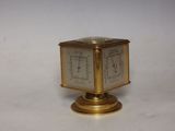 a small brass clock on a stand on a white surface