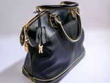 black leather handbag with gold zippers sitting on a white surface
