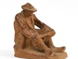 figurine of a man sitting on a rock with a hat on