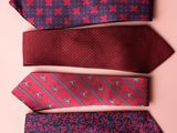 four ties are lined up in a row on a pink surface