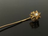 a close up of a gold brooch with a pearl in the center