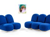 pair of blue lounge chairs in front of a painting of a man ' s face