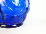un vase en verre bleu avec un socle noir posé sur une surface blanche