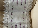 purple flowers are embroidered on a white table runner on a beige couch