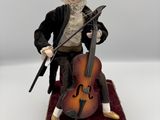 une figurine représentant un homme avec un violoncelle posé sur une boîte